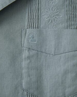 The pocket of a grey Dandy Del Mar Brisa Linen Shirt with embroidered flowers.