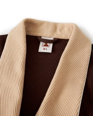 Close-up of The Cannes Waffle Knit Robe - Carajillo by Dandy Del Mar, a brown garment with a beige textured collar in waffle knit fabric, featuring an M/L size tag.