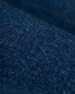 Close-up image of indigo denim fabric from The Cartagena Denim Shirt by Dandy Del Mar, displaying detailed texture with visible weave patterns and tailored fit features.