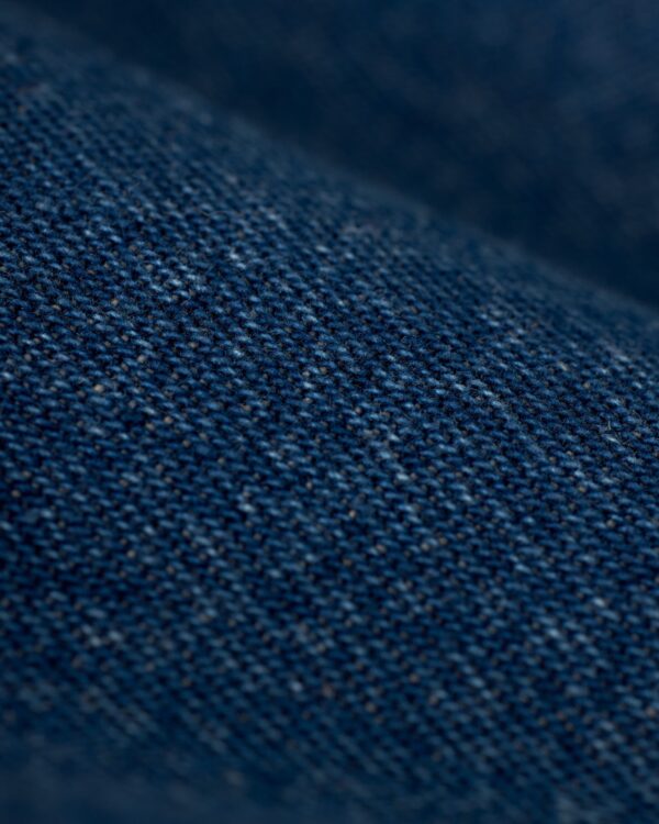 Close-up image of indigo denim fabric from The Cartagena Denim Shirt by Dandy Del Mar, displaying detailed texture with visible weave patterns and tailored fit features.