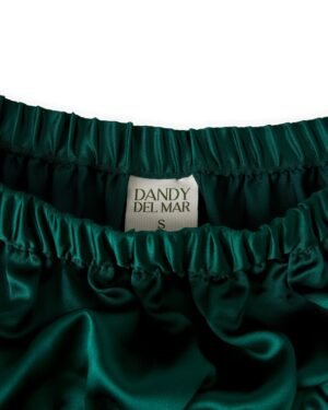 Close-up of a dark green satin garment with an elastic waistband, displaying a label reading 