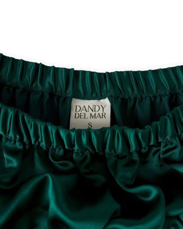 Close-up of a dark green satin garment with an elastic waistband, displaying a label reading "The Monaco Maxi Skirt - Albero by Dandy Del Mar, Size S".