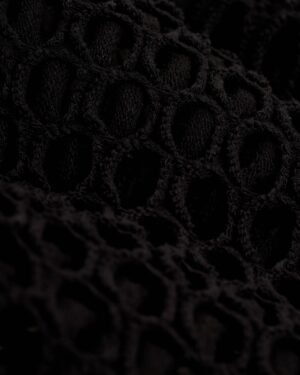 Close-up of a black, textured, open-knit fabric with a repeating pattern of oval-shaped holes, perfect for The Montserrat Crochet Skirt - Onyx by Dandy Del Mar.