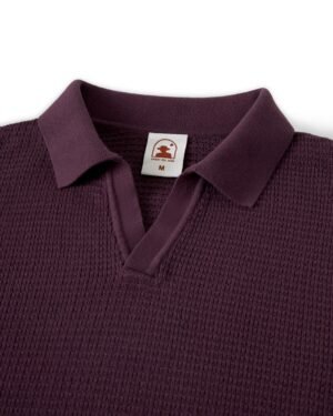 A close-up of The Sebastian Long Sleeve Polo in Amethyst by Dandy Del Mar highlights its textured sweater-knit cotton finish, with a label inside the collar displaying a logo and the letter 