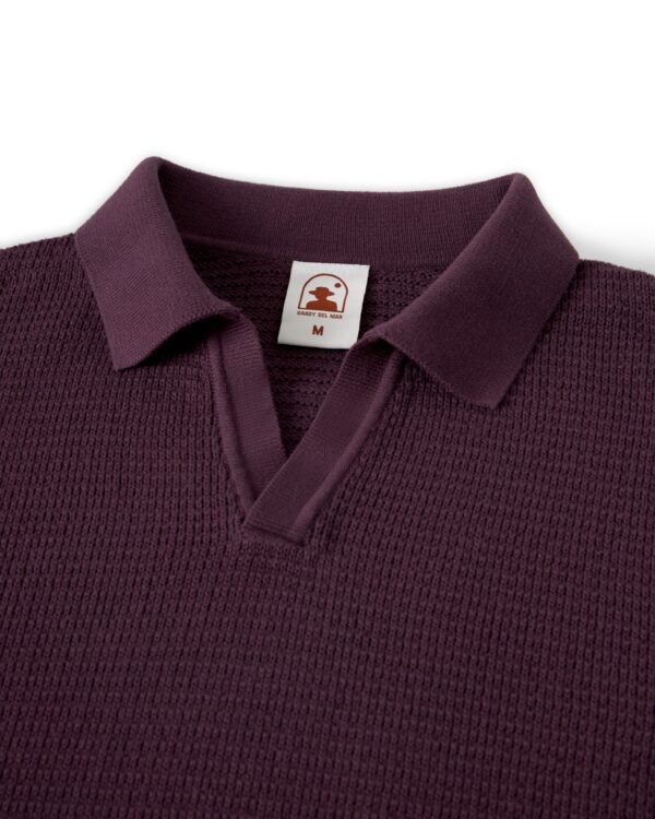 A close-up of The Sebastian Long Sleeve Polo in Amethyst by Dandy Del Mar highlights its textured sweater-knit cotton finish, with a label inside the collar displaying a logo and the letter "M".