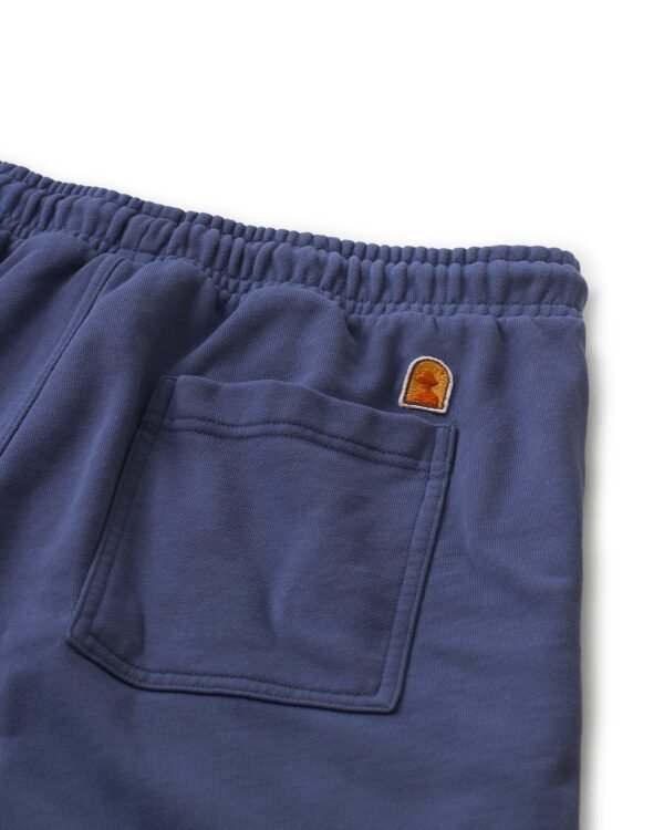 Close-up of The Marseille French Terry Short in Moontide by Dandy Del Mar, showcasing a blue design with an elastic waistband and a back pocket. Made from soft French terry fabric, it features a small brown and orange embroidered patch above the pocket.