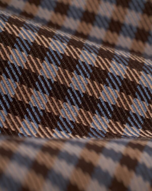 Close-up of a textile with a checkered pattern in brown, blue, and beige colors, resembling the intricate design of The Tresco Trouser - Tierra Houndstooth by Dandy Del Mar.