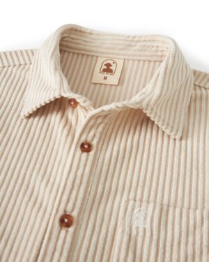 Close-up of The Tropez Jacquard Shirt - Scallop Stripe from Dandy Del Mar, featuring brown buttons, a chest pocket with an embroidered logo, and a size tag marked 