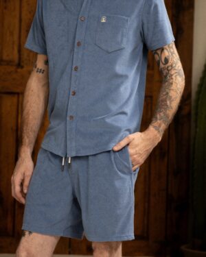 A person is sporting a blue button-up shirt and The Tropez Short - Annapolis by Dandy Del Mar, revealing their arm tattoos.