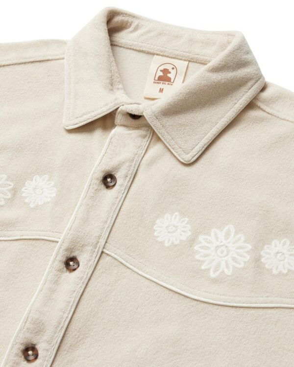 The Gaucho Shirt - Alabaster by Dandy Del Mar is a beige collared shirt with exquisite flower embroidery and brown buttons, blending rugged style with elegance.